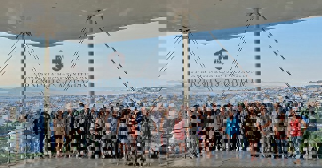 A large group poses for a photo at the Stavros Niarchos Foundation Cultural Center, overlooking Athens