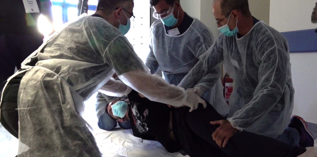 Four people in surgical gowns and masks practice a technique on a volunteer lying on their side