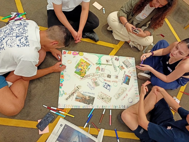 Καθιστοί νέοι χρησιμοποιούν μαρκαδόρους για να δημιουργήσουν μια πολύχρωμη αφίσα