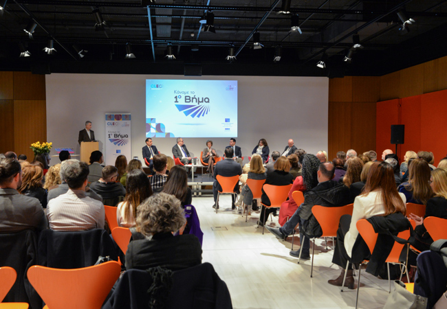 A diverse crowd of people sitting in an event hall, watching a presentation.
