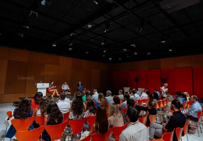Seated audience attending a panel of three people in a large room.
